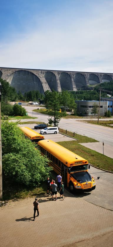 Des bus scolaires jaunes stationnés près d'un barrage sous un ciel bleu.