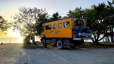 Un véhicule de voyage orange au bord de la mer au coucher du soleil.