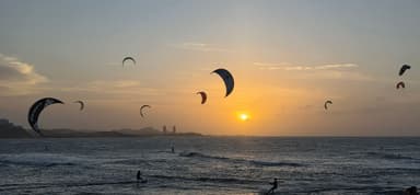 Kitesurfers on the ocean at sunset with a colorful sky.