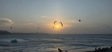 A sunset over the ocean with kite surfers and silhouettes on the beach.