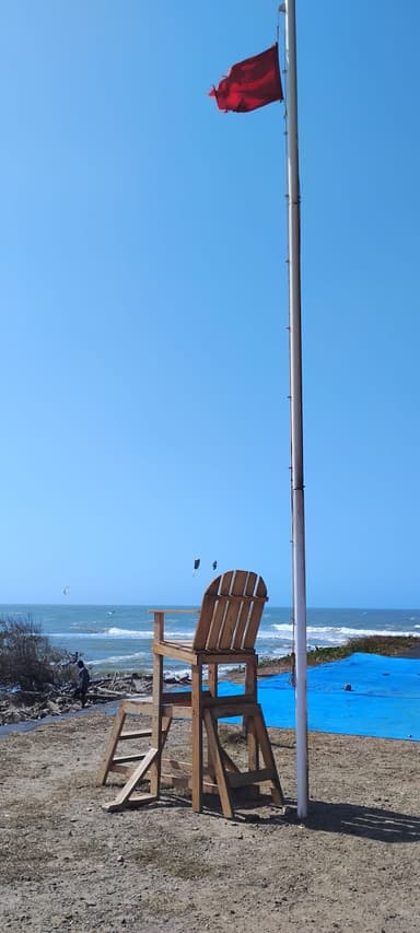 A lifeguard chair beside a red flag on a beach with waves in the background.