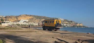 Un camion jaune sur la plage avec des montagnes en arrière-plan.