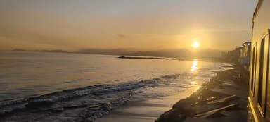 Un coucher de soleil sur la mer à Lechería, avec des vagues douces et des montagnes en arrière-plan.