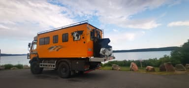 Un véhicule orange stationné près d'un lac sous un ciel nuageux.