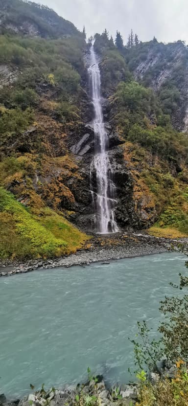 Une cascade se déverse dans une rivière turquoise entourée de verdure.