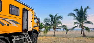 Un camion jaune près de la plage avec des palmiers.
