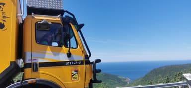 Un camion jaune surplombe l'océan et les collines verdoyantes.