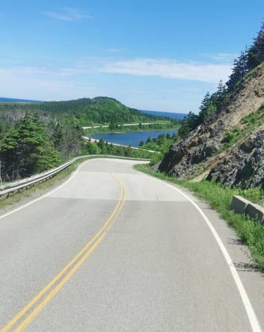 Une route sinueuse avec des collines verdoyantes et un lac en arrière-plan.