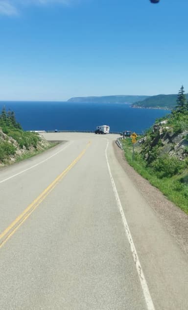 Une route sinueuse avec vue sur l'océan et des collines verdoyantes.