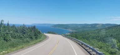Une route sinueuse avec vue sur la mer et les collines verdoyantes.