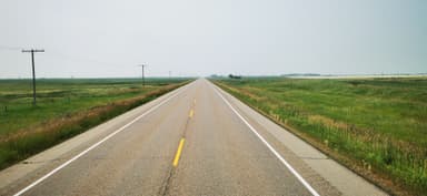 Une route droite à travers des prairies verdoyantes sous un ciel brumeux.