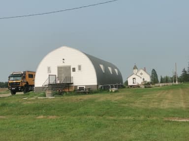 Une grange moderne et une maison blanche sur un terrain vert.