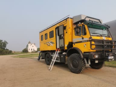 Un camion jaune stationné près d'un bâtiment blanc dans un paysage rural.