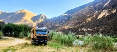 Un camion orange dans un paysage montagneux ensoleillé.