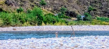 Un homme pêche près d'une rivière entourée de rochers et de verdure.