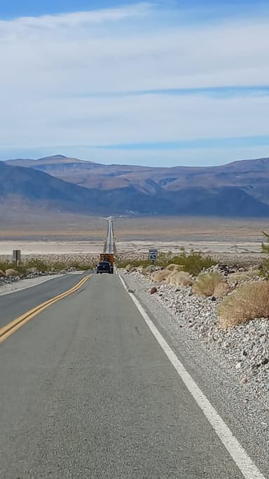 Une route s'étend vers des montagnes sous un ciel bleu.