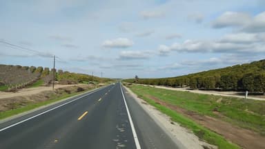 Une route bordée d'arbres et de collines sous un ciel nuageux.