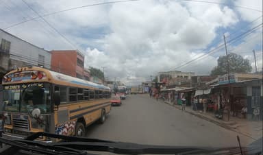 Une rue animée avec des bus et des magasins sous un ciel nuageux.