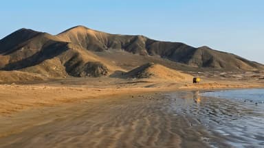 Une plage avec des montagnes en arrière-plan et un véhicule au loin.