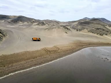 Un véhicule orange sur une plage désertique avec des collines en arrière-plan.