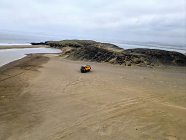 Un véhicule orange sur une plage désertique à Huacho, sous un ciel nuageux.