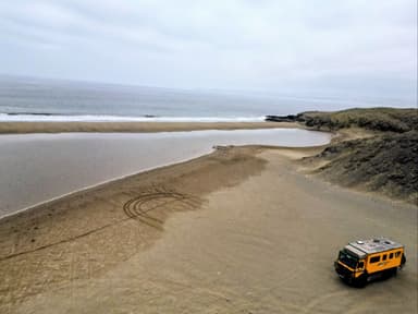 Un paysage de plage avec un véhicule sur le sable et l'océan en arrière-plan.