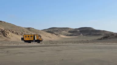 Un véhicule jaune sur une plage désertique avec des collines en arrière-plan.