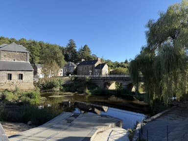 Un paysage de La Gacilly avec un pont et des maisons au bord de l'eau.