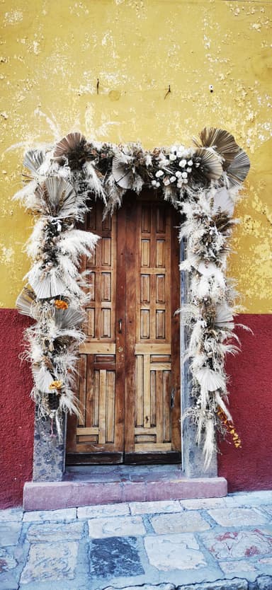 Une porte en bois décorée de fleurs sèches sur un mur jaune.