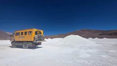 Un véhicule tout-terrain jaune sur un paysage désertique blanc sous un ciel bleu.