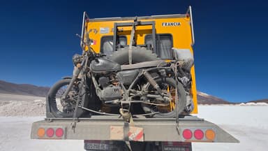 Un camion jaune transportant une moto sur un fond désertique.