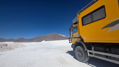 Un camion jaune sur un paysage désertique avec des montagnes au loin.