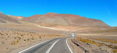 Une route sinueuse à travers un paysage désertique avec des montagnes en arrière-plan.