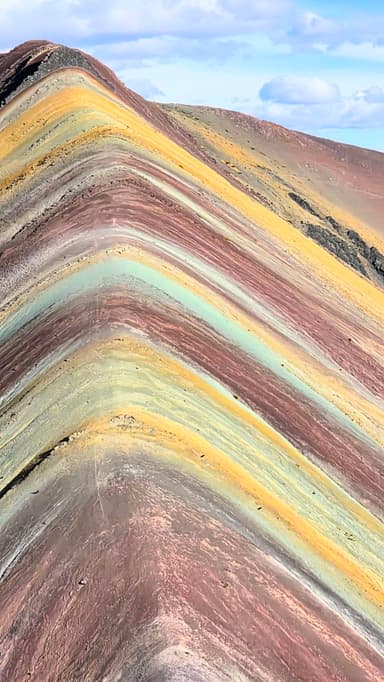 Une vue des montagnes colorées à Cusipata, avec des strates de couleurs vives sous un ciel nuageux.