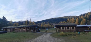 Deux bâtiments en bois entourés de nature et de montagnes sous un ciel bleu.