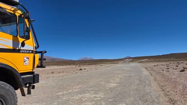 Un camion jaune sur une route désertique sous un ciel bleu.