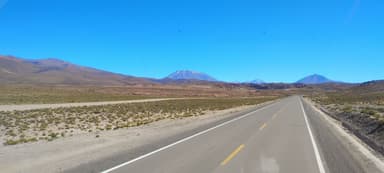 Une route déserte avec des montagnes au loin sous un ciel bleu.