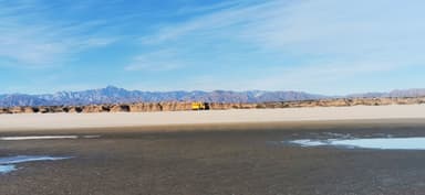 Un paysage désertique avec des montagnes au loin et un véhicule jaune sur la plage.