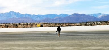 Un homme marche sur une plage avec des montagnes en arrière-plan.