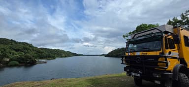 Un camion jaune près d'un lac entouré de verdure sous un ciel nuageux.