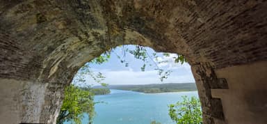 Une vue à travers une arche de pierre sur une rivière entourée de verdure.