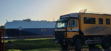 Un camion jaune et un grand navire au port sous un ciel clair.