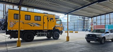 Un camion jaune et une voiture sous un abri, avec des conteneurs en arrière-plan.