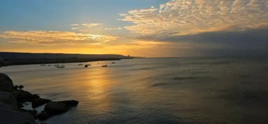 Un coucher de soleil sur l'eau avec des bateaux au loin.
