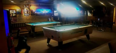 Une salle de jeux avec des tables de billard et un éclairage tamisé.