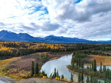 Un paysage d'Alaska avec des montagnes et une rivière entourée d'arbres aux couleurs d'automne.