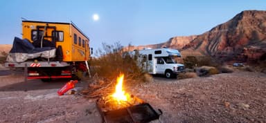 Un feu de camp avec des camping-cars dans un paysage désertique au crépuscule.