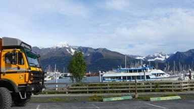 Un paysage de marina avec des montagnes en arrière-plan et un camion jaune au premier plan.