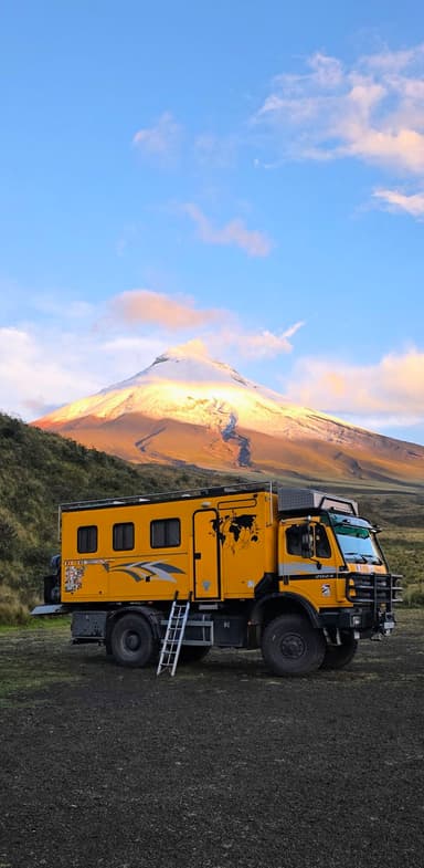 Un camion jaune devant une montagne sous un ciel bleu.