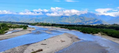 Un paysage de rivière entouré de montagnes sous un ciel bleu.